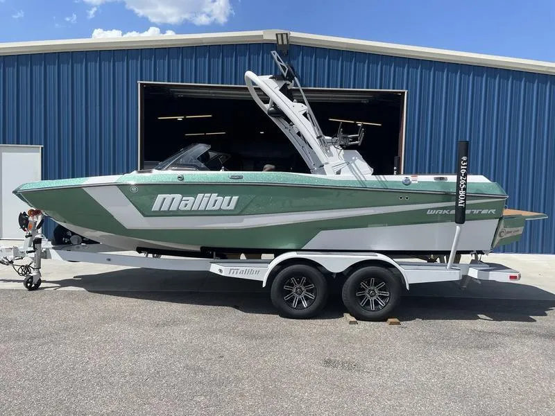 Slide: The Image of 2024 Malibu 21 LX boat on trailer in front of blue warehouse. - 0