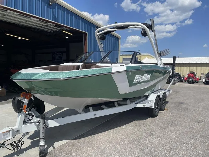 Slide: The Image of 2024 Malibu 21 LX boat on trailer outside a blue warehouse. - 1