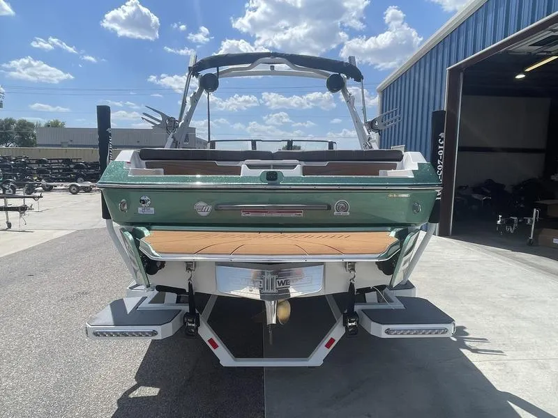 Slide: The Image of 2024 Malibu 21 LX boat, rear view, docked outside a blue warehouse. - 13