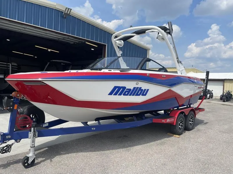 Slide: The Image of 2024 Malibu 22 LSV boat in red, white, and blue on a trailer outside a blue warehouse. - 2