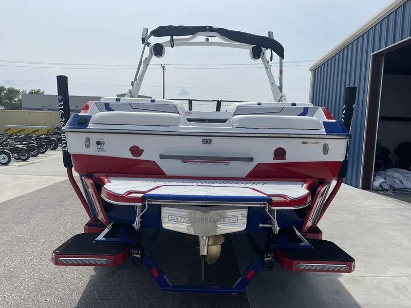 Slide: The Image of 2024 Malibu 22 LSV boat, rear view, parked outside a blue building. - 6