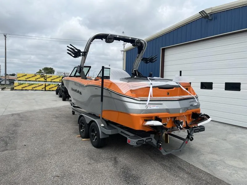Slide: The Image of 2024 MasterCraft NXT23 boat in orange and gray, parked outside a blue warehouse. - 4