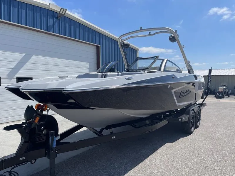 Slide: The Image of 2023 Malibu 24 MXZ boat on trailer outside a blue warehouse. - 2