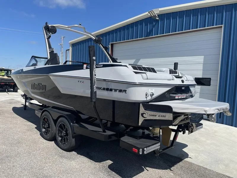 Slide: The Image of 2023 Malibu 24 MXZ boat on trailer outside blue building. - 4