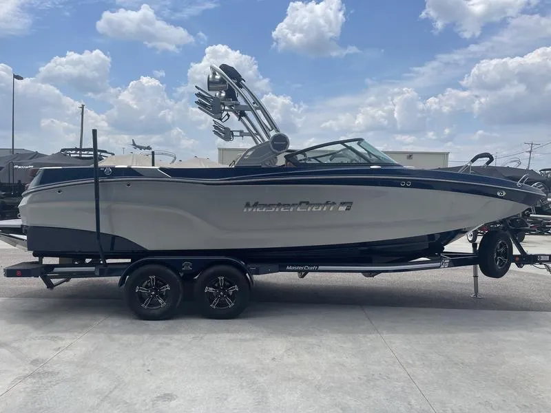 Slide: The Image of 2023 MasterCraft XT24 boat on trailer under a cloudy sky. - 1