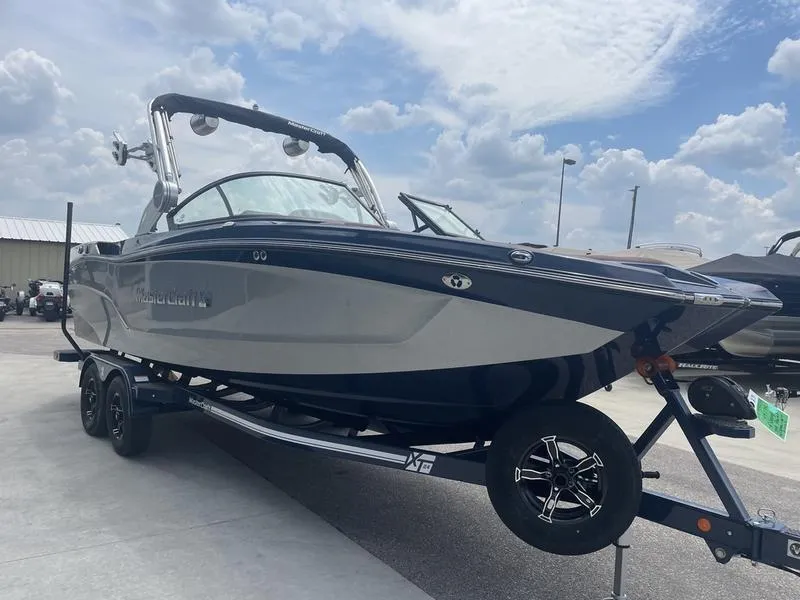 Slide: The Image of 2023 MasterCraft XT24 boat on trailer under cloudy sky. - 2