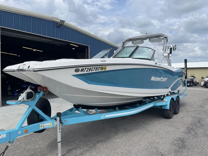 Slide: The Image of 2019 MasterCraft X26 boat on a trailer outside a blue warehouse. - 2