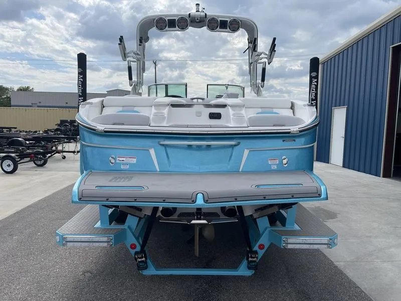 Slide: The Image of 2019 MasterCraft X26 boat, rear view, blue exterior, docked near blue building. - 5
