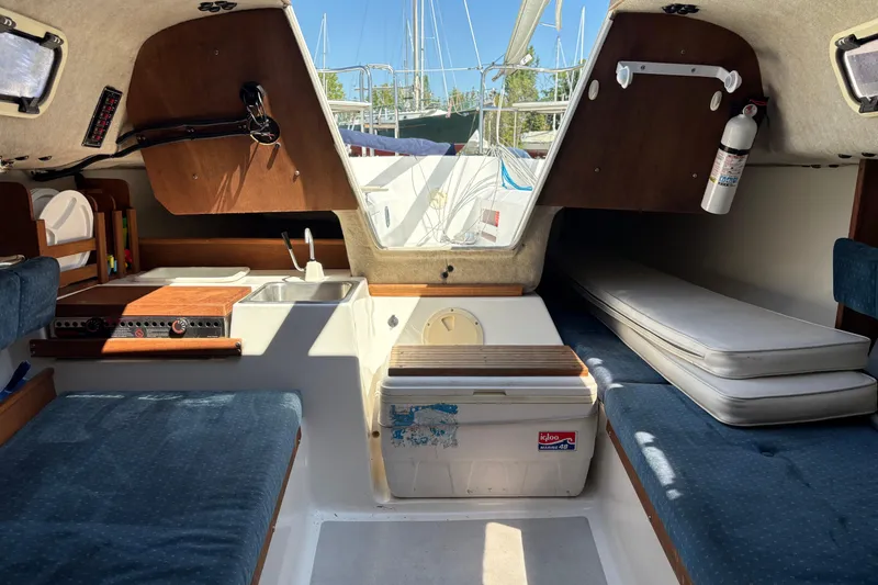 Slide: The Image of Interior of a 2002 Precision 23 sailboat, featuring seating, a sink, and a fire extinguisher. - 22