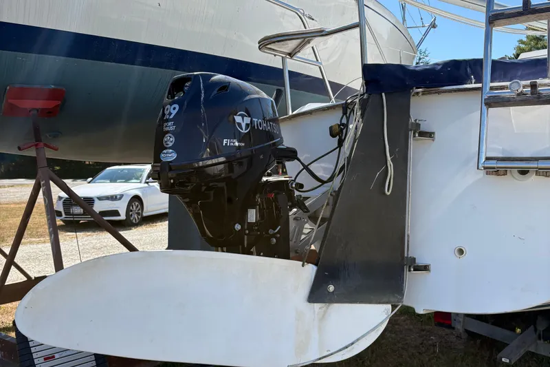 Slide: The Image of Outboard motor on a 2002 Precision 23 sailboat, parked with other boats and a car nearby. - 7