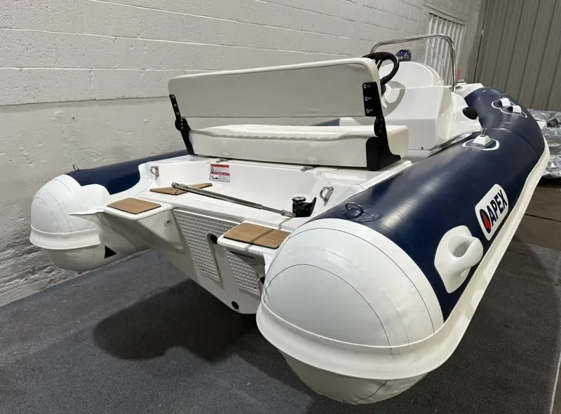 Slide: The Image of 2024 Apex A-13 Deluxe Tender, inflatable boat with white and navy design, in indoor setting. - 2
