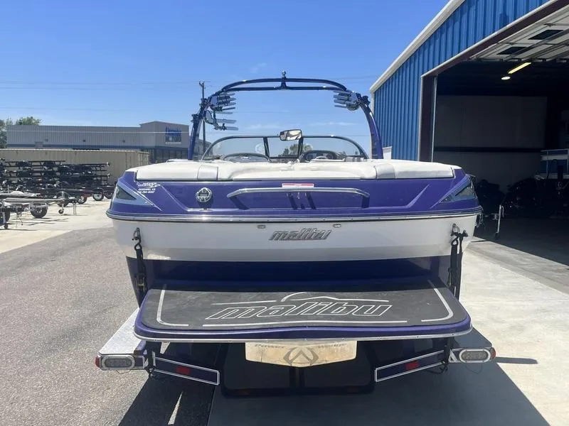 Slide: The Image of 2007 Malibu 247 LSV boat, rear view, parked outside a blue warehouse. - 6
