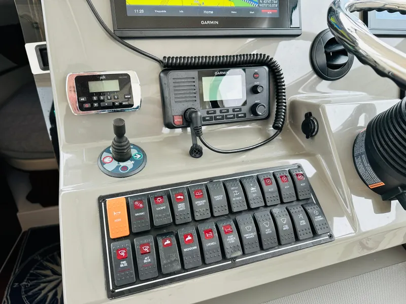 Slide: The Image of Control panel of a 2017 Pursuit OS 355 boat with various switches and navigation equipment. - 17