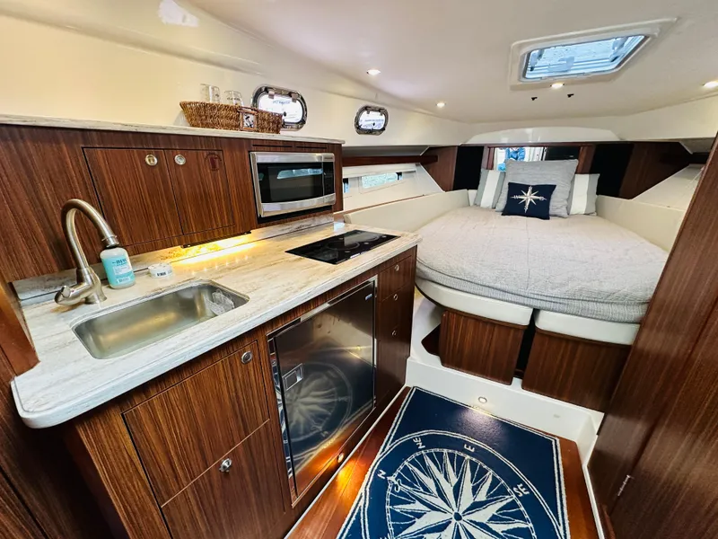 Slide: The Image of 2017 Pursuit OS 355 cabin interior with kitchenette, bed, and nautical-themed decor. - 28