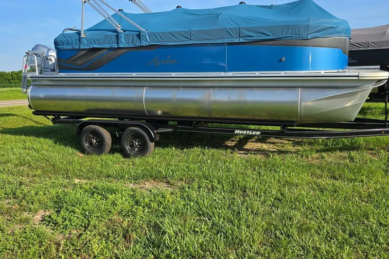 Slide: The Image of 2024 Avalon VLS Quad Lounger pontoon boat on trailer, covered and parked on grass. - 0