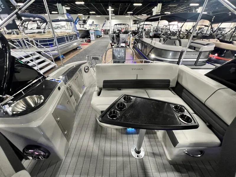 Slide: The Image of Interior of 2024 Sylvan G5 CLZ DC Arch Tritoon with seating and table at a boat show. - 33