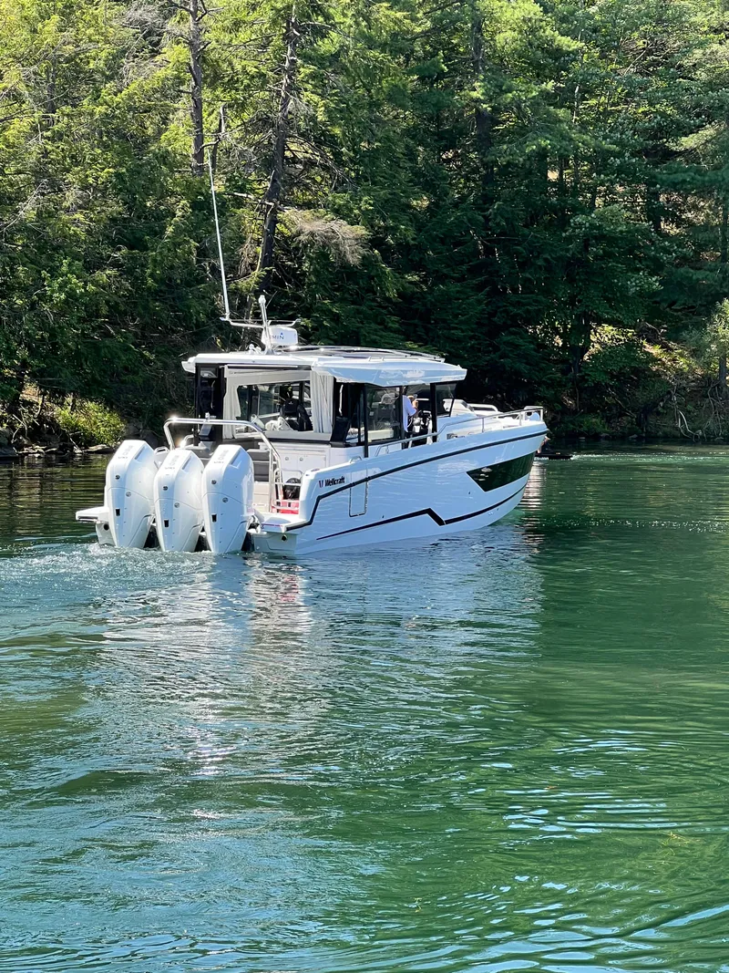Slide: The Image of 2024 Wellcraft 355 Commuter boat cruising on a serene lake surrounded by trees. - 1