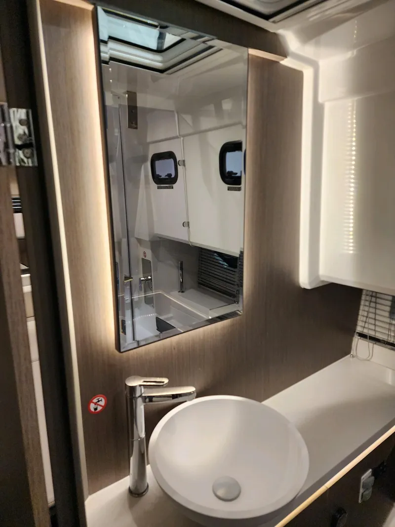 Slide: The Image of 2024 Wellcraft 355 Commuter bathroom with modern sink, mirror, and porthole windows. - 6