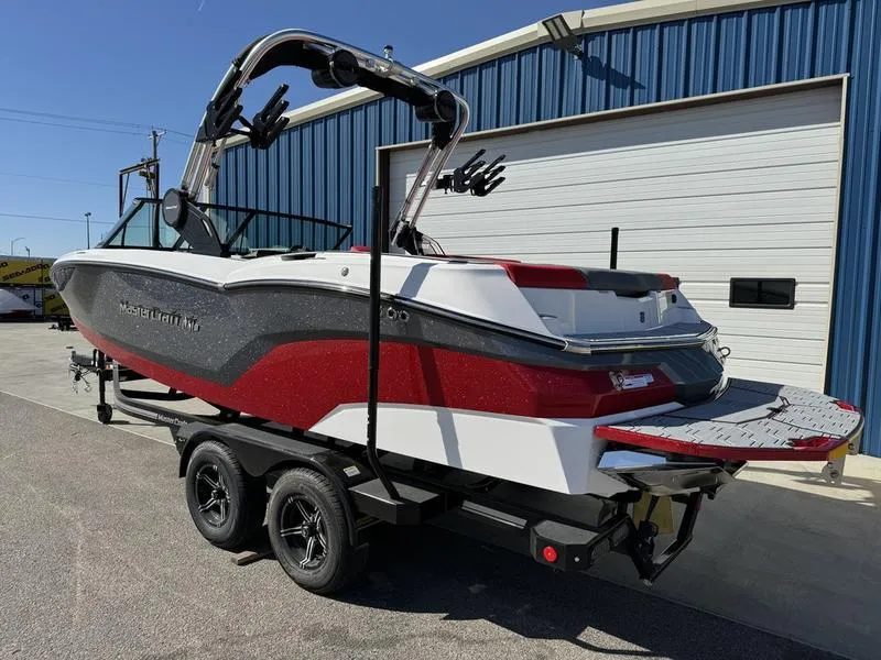 Slide: The Image of 2024 MasterCraft NXT 22 boat on trailer, red and white, parked outside blue building. - 7