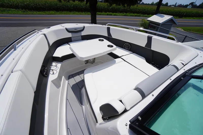 Slide: The Image of 2025 Chaparral 280 OSX boat interior with white seating and table, near a road and greenery. - 20