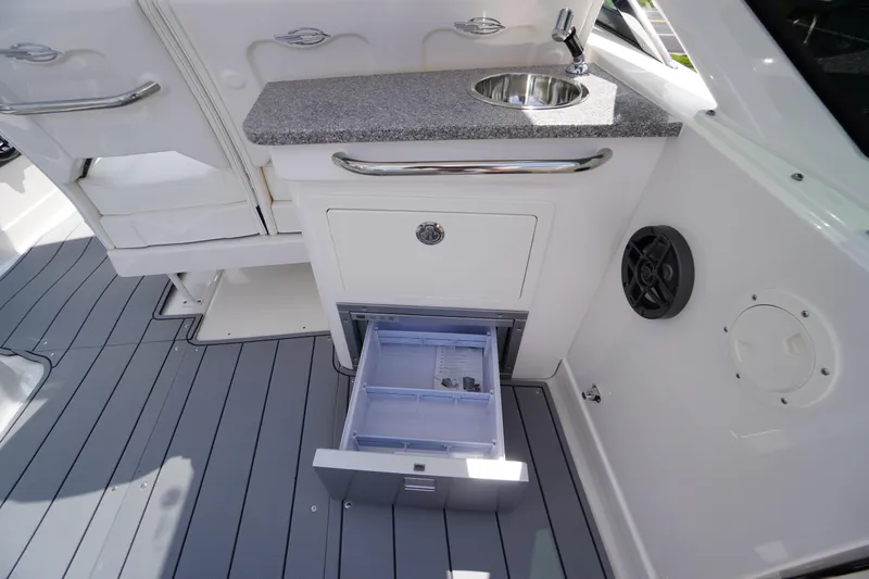Slide: The Image of 2025 Chaparral 280 OSX boat interior with sink, storage, and open drawer on sleek deck. - 34
