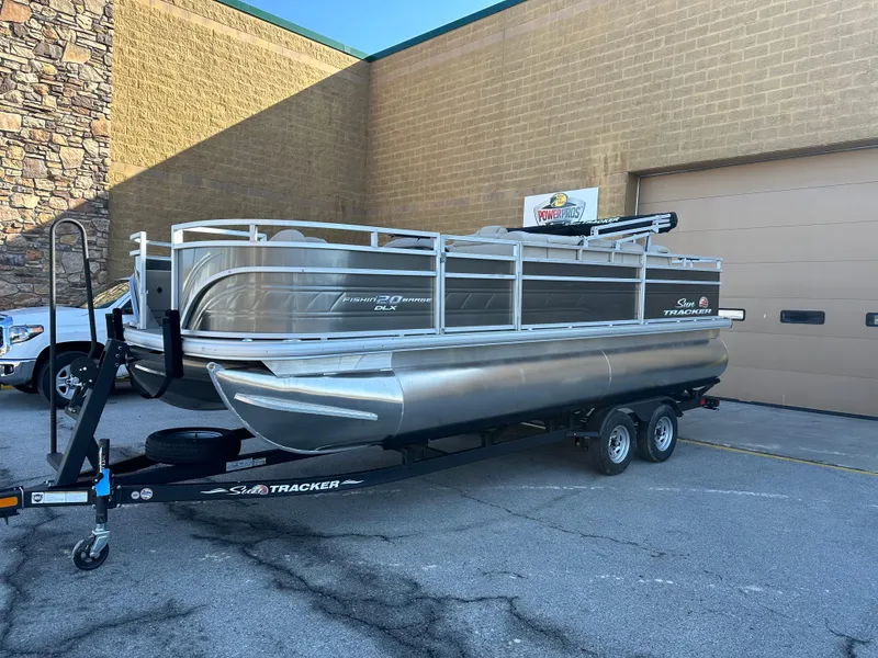 The Image of 2024 Sun Tracker Fishin' Barge 20 DLX pontoon boat on trailer outside a building. - 0