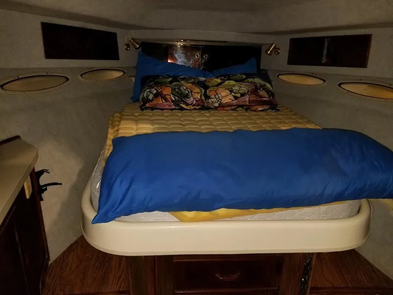Slide: The Image of 1986 Sea Ray 390 Express cabin with bed, colorful bedding, and porthole windows. - 19