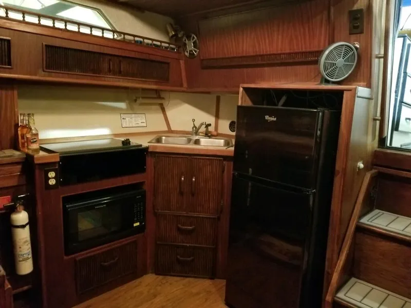 Slide: The Image of 1986 Sea Ray 390 Express yacht kitchen with microwave, fridge, sink, and wooden cabinetry. - 24