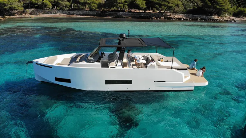 The Image of 2024 De Antonio Yachts D42 Open cruising in clear turquoise waters near a forested shoreline. - 1