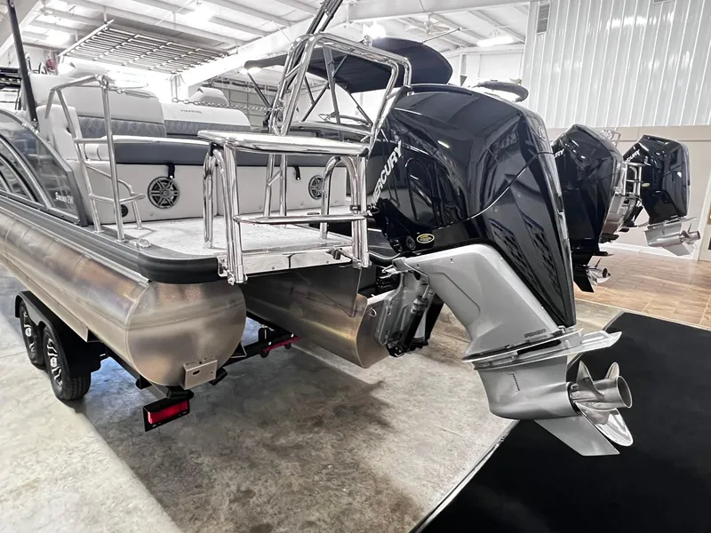 Slide: The Image of 2024 Harris Sunliner 230 pontoon boat with dual Mercury outboard engines in a showroom. - 28