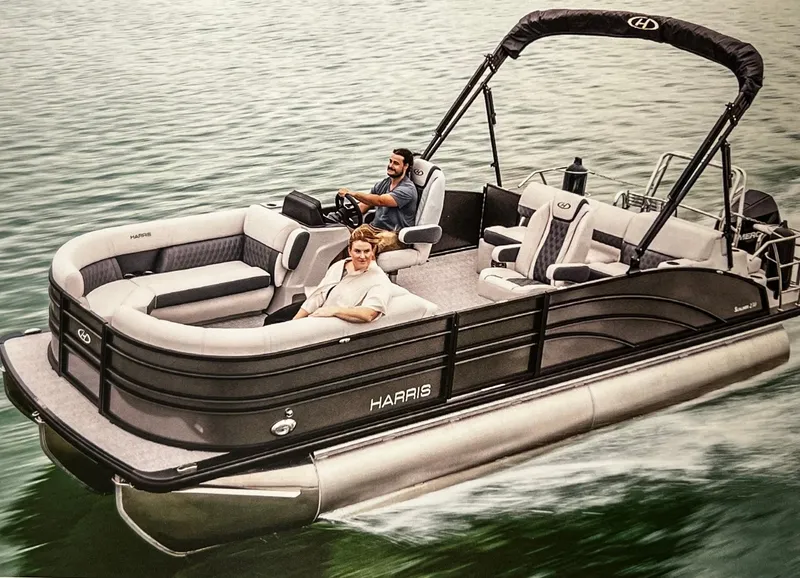 Slide: The Image of 2024 Harris Sunliner 230 pontoon boat cruising on water with two passengers. - 36