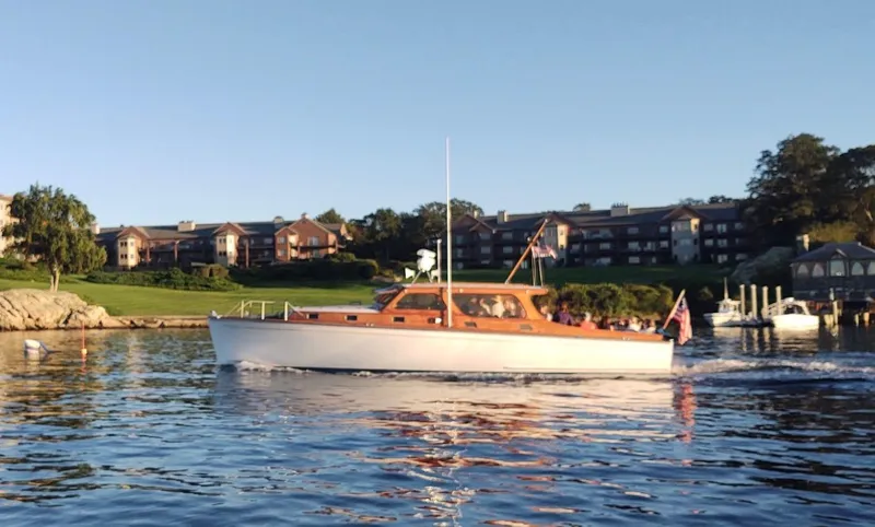 The Image of 1947 Rhodes Nevins Picnic Boat cruising on a serene lake near waterfront homes. - 0