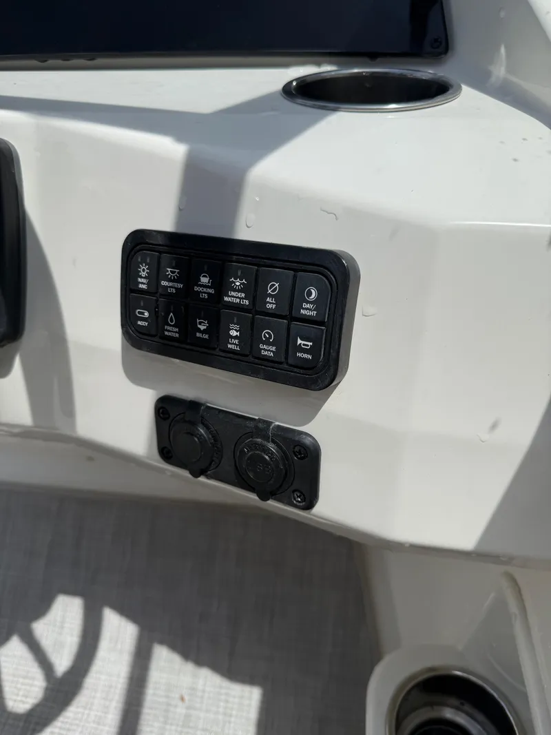 Slide: The Image of Control panel on 2024 Stingray 201DC boat dashboard with various switches and cup holder. - 14