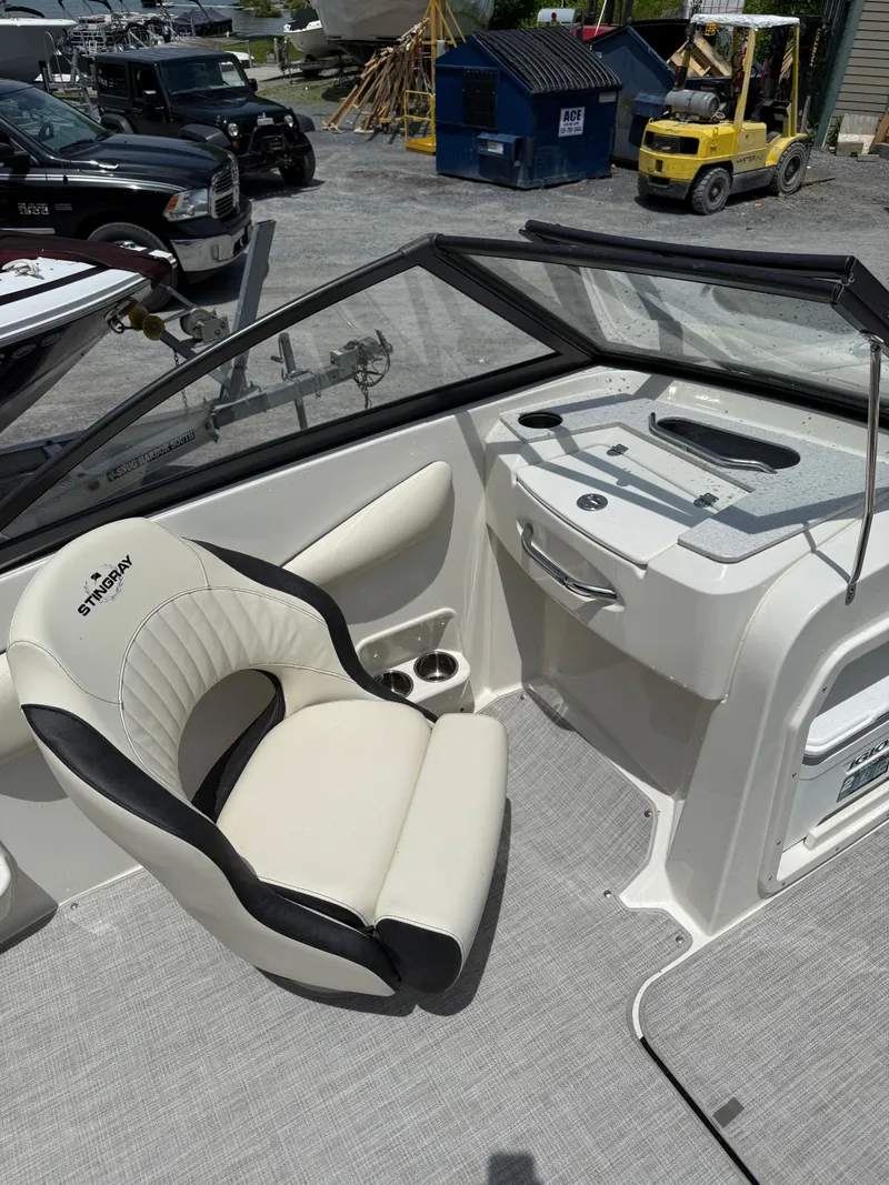 Slide: The Image of 2024 Stingray 201DC boat interior with white seating and dashboard, parked outdoors. - 17