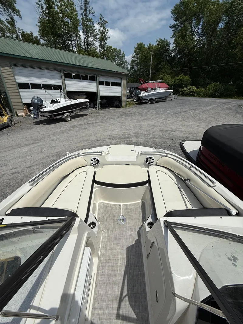 Slide: The Image of 2024 Stingray 201DC boat interior with seating, parked near a garage and other boats. - 21