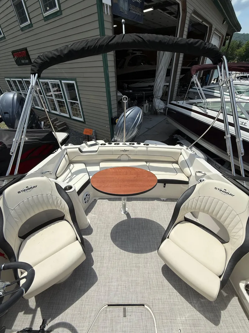 Slide: The Image of 2024 Stingray 201DC boat interior with seating and table, docked near a building. - 27