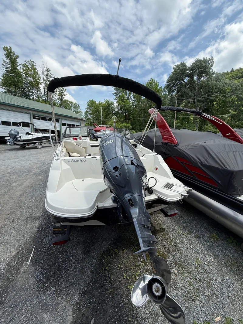 Slide: The Image of 2024 Stingray 201DC boat with outboard motor, parked outdoors under cloudy sky. - 5