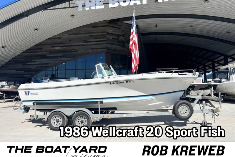 The Image of 1986 Wellcraft V-20 Sport boat on trailer at dealership, American flag displayed. - 0
