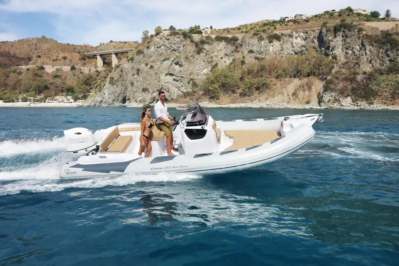 Slide: The Image of 2025 Ranieri Cayman 23.0 Sport Touring boat cruising on blue water near rocky coastline. - 14