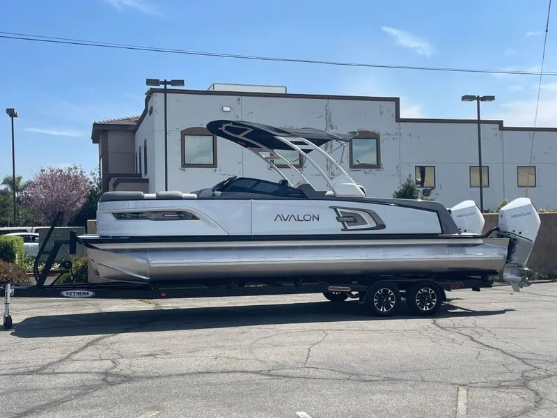 The Image of 2024 Avalon 2585 EXCALIBUR LTD VRB pontoon boat on a trailer in a parking lot. - 1