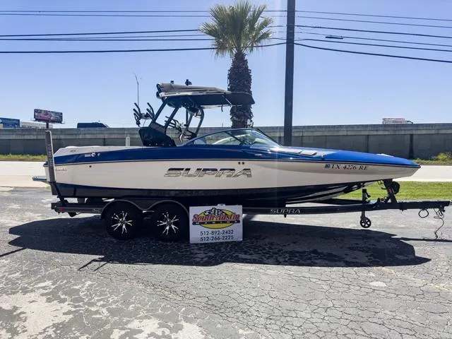 The Image of 2013 Supra SA 350 boat on trailer, blue and white design, parked outdoors. - 1