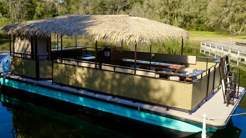Slide: The Image of 2024 A&M Manufacturing BullDog 34 pontoon boat with a thatched roof on a serene lake. - 10