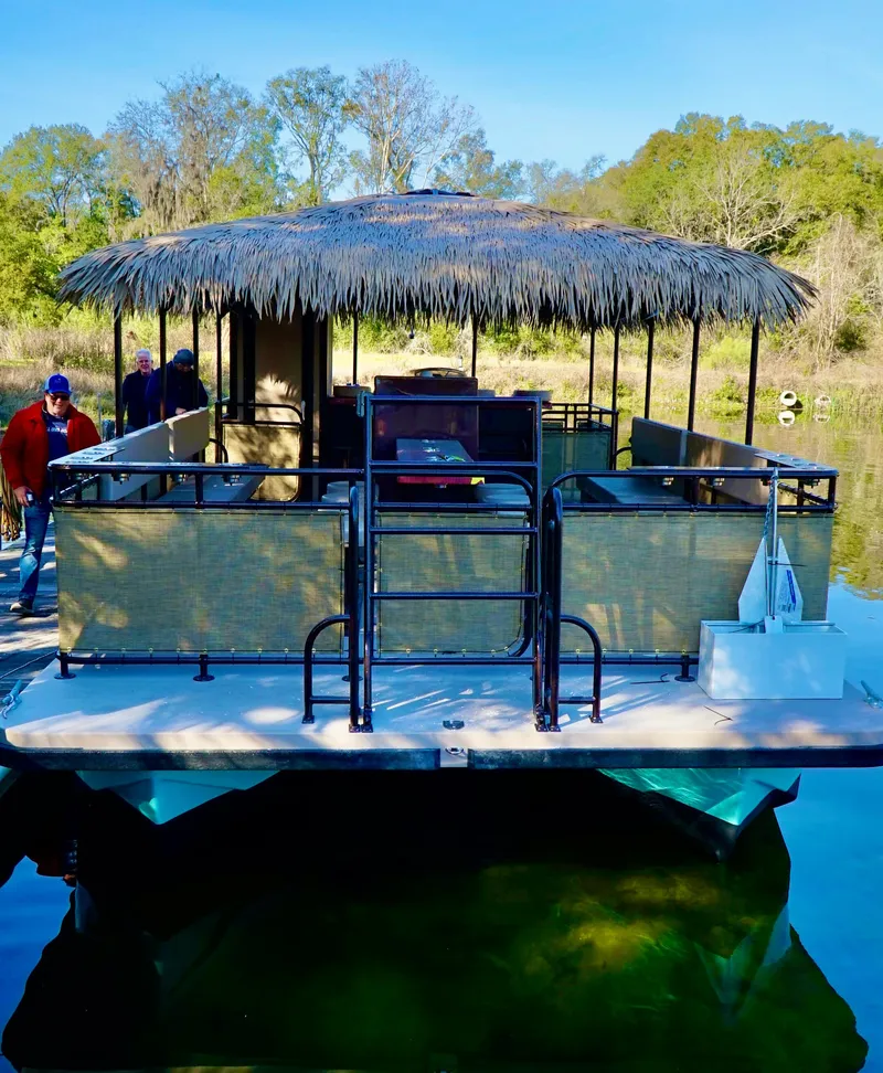 Slide: The Image of 2024 A&M Manufacturing BullDog 34 pontoon boat with a thatched roof on a serene lake. - 16