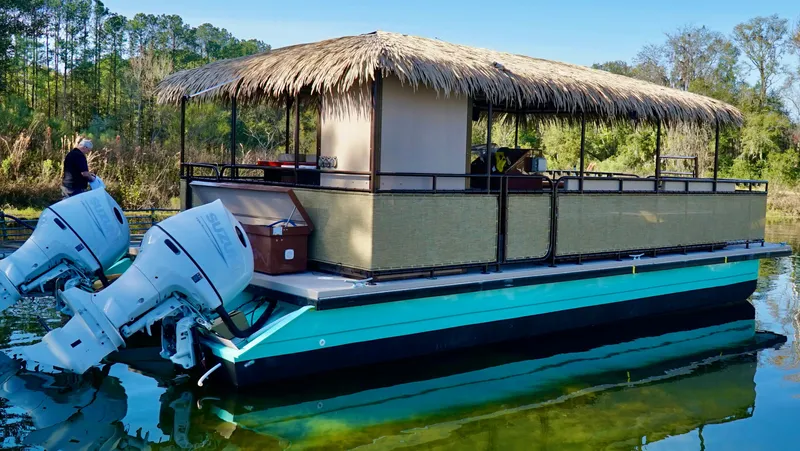 Slide: The Image of 2024 A&M Manufacturing BullDog 34 pontoon boat with twin outboard motors and a thatched roof. - 7
