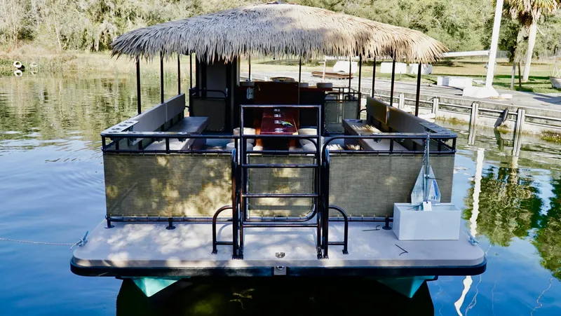 Slide: The Image of 2024 A&M Manufacturing BullDog 34 pontoon boat with thatched roof on calm water. - 8