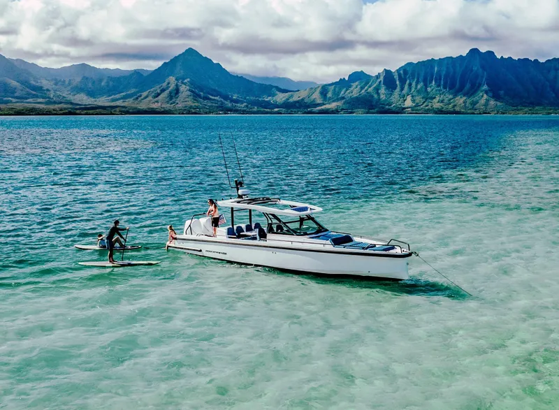 Slide: The Image of 2024 Axopar 37 Sun Top in turquoise waters with paddleboarders, scenic mountain backdrop. - 6