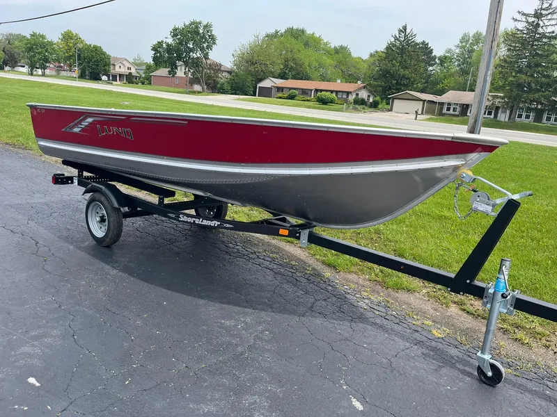 Slide: The Image of 2024 Lund WC-14 boat on trailer, red and silver, parked on asphalt. - 3
