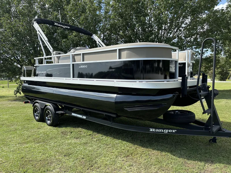 Slide: The Image of 2024 Ranger 200C pontoon boat on trailer, parked on grass with trees in background. - 3