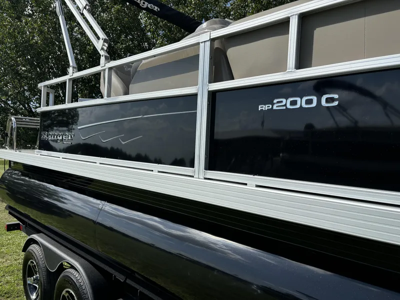 Slide: The Image of 2024 Ranger 200C pontoon boat, black exterior, parked on a trailer. - 4