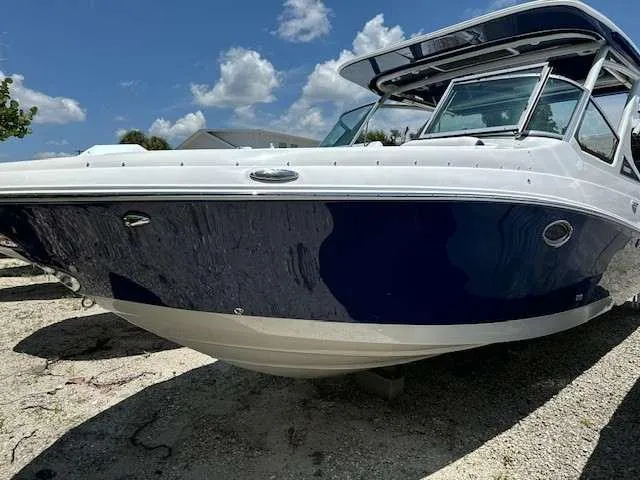 Slide: The Image of 2024 Crownline 280 DC boat with sleek design, parked on sandy ground under blue sky. - 2